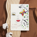 A hand-drawn portrait of a woman with closed eyes, red lips, and golden eye shadow. A brightly coloured butterfly, red, yellow, blue, and green, rests near her temple, surrounded by soft green heart shapes and abstract black lines. In red handwritten text, it reads: “THE WOMAN. Here you ARE, moving ahead bravely despite everything that went wrong.” The artwork is emotive and hopeful, honouring resilience, beauty, and quiet strength.