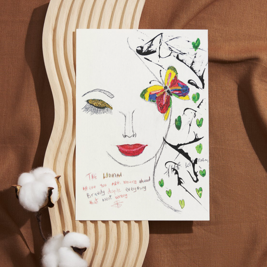 A hand-drawn portrait of a woman with closed eyes, red lips, and golden eye shadow. A brightly coloured butterfly, red, yellow, blue, and green, rests near her temple, surrounded by soft green heart shapes and abstract black lines. In red handwritten text, it reads: “THE WOMAN. Here you ARE, moving ahead bravely despite everything that went wrong.” The artwork is emotive and hopeful, honouring resilience, beauty, and quiet strength.